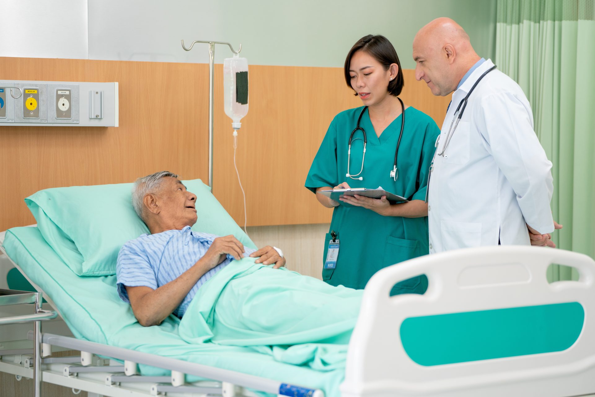 Doctor and nurse talk with elderly patient in hospital